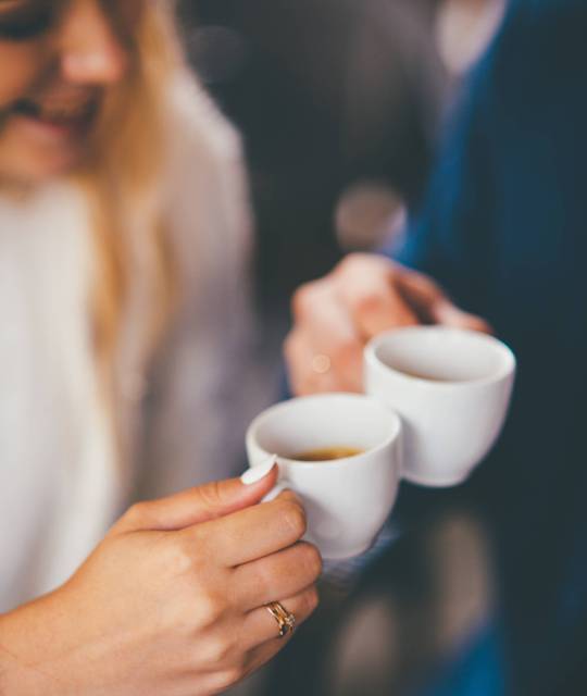 Close up shot of smiling couple holding small white cups in their hands